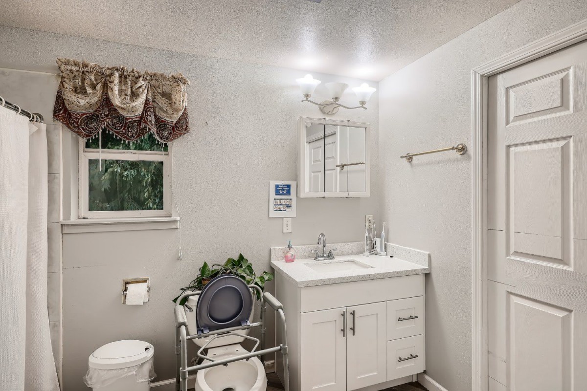 A bathroom with a toilet, sink, mirror, and medical equipment.