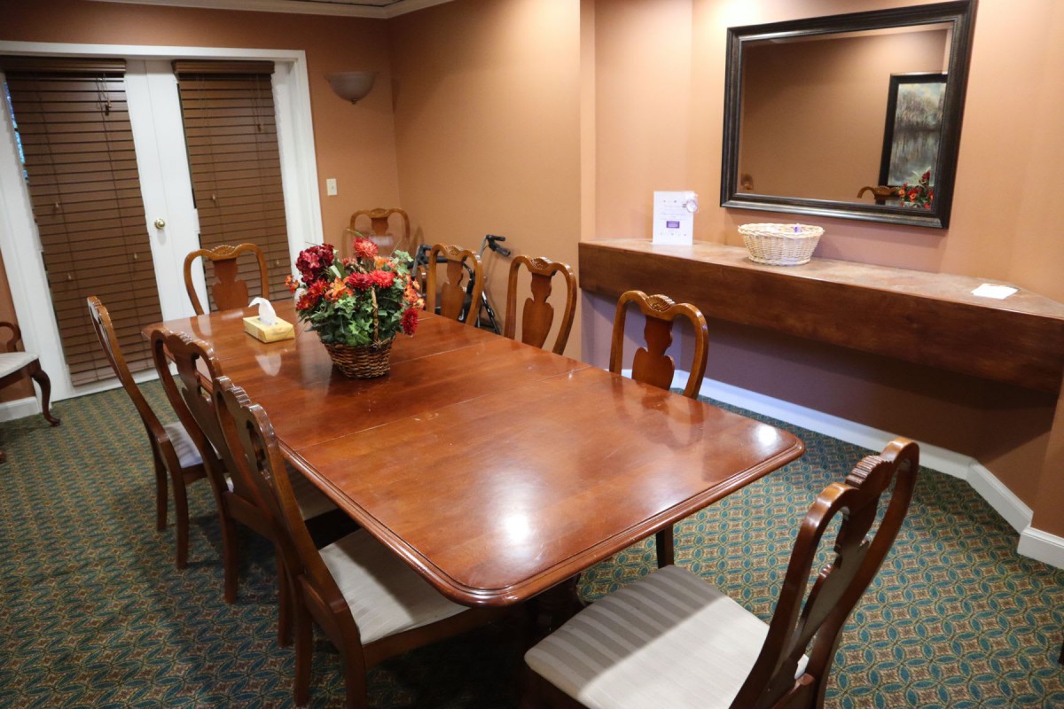 A well-furnished dining room with a polished wood table and chairs, decorated with flowers.