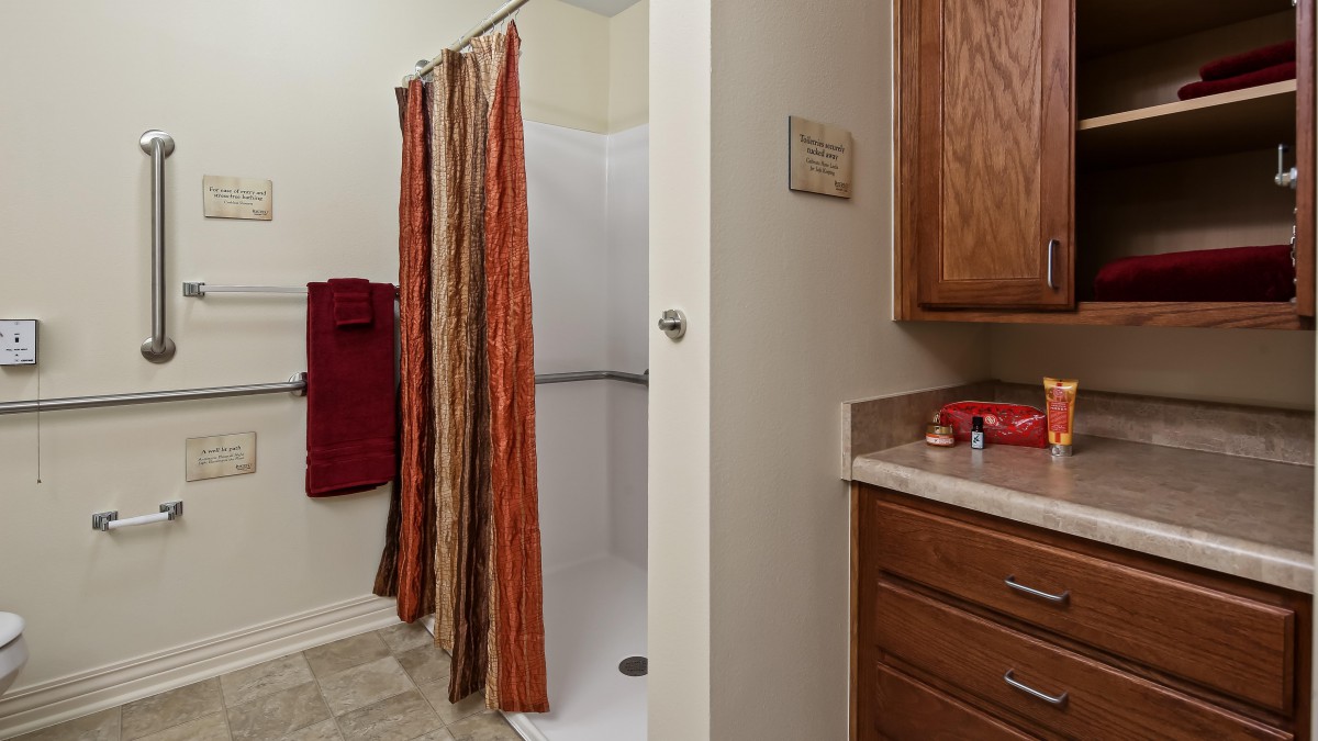 A bathroom featuring a shower with striped curtains, red towels, and a wooden cabinet.