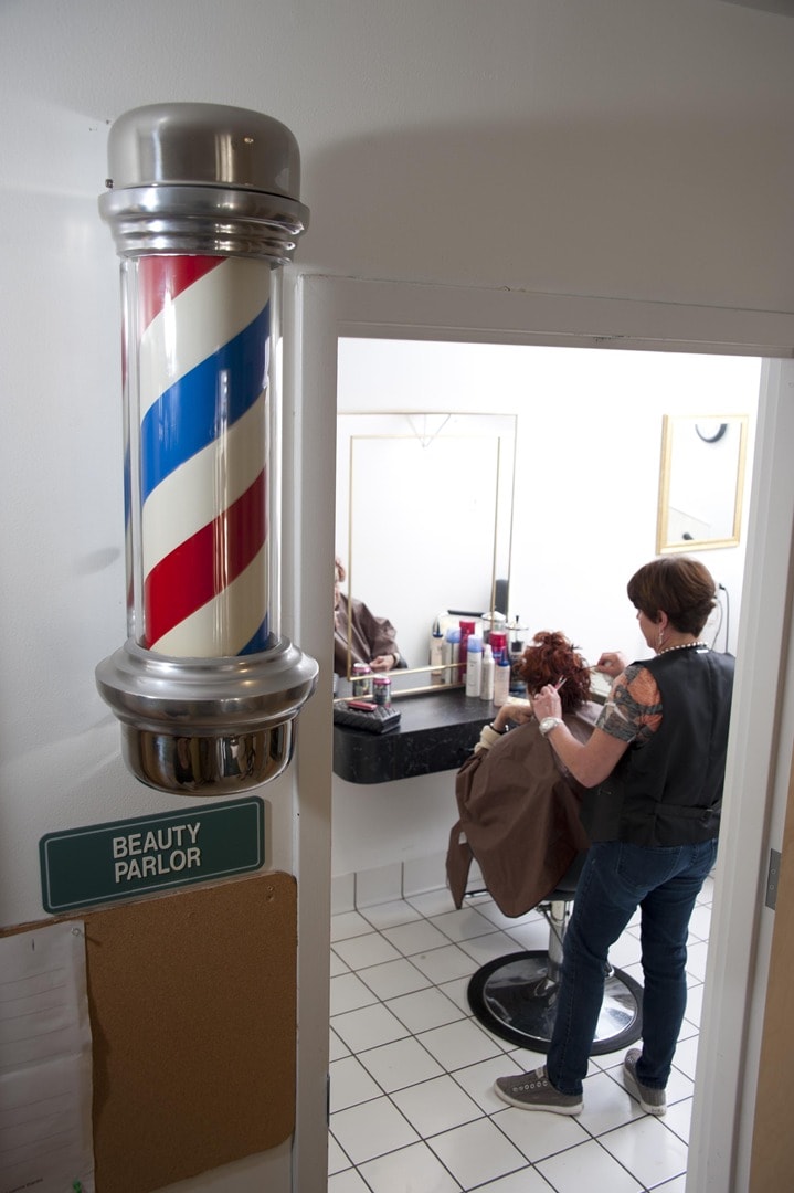 A barber gives a haircut to a customer in a salon with a traditional barber pole at the entrance.