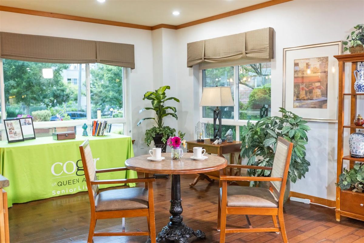 A cozy dining area with a wooden table and chairs, surrounded by plants and natural light from large windows.