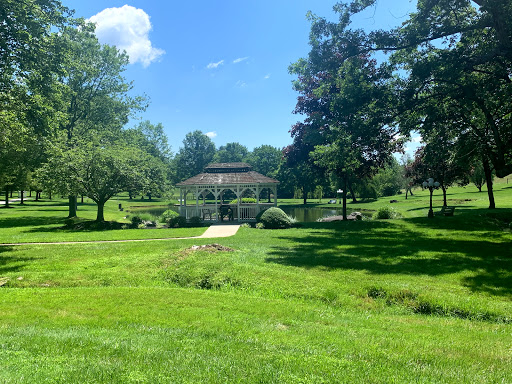 A serene park scene featuring a gazebo surrounded by lush greenery under a clear blue sky.