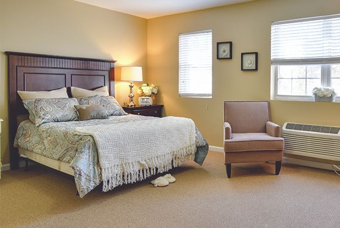 A cozy bedroom featuring a neatly made bed, an armchair, and warm lighting.