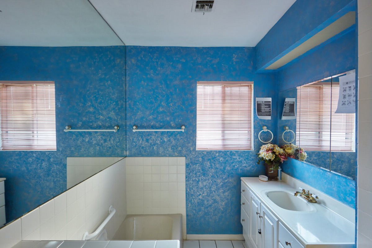 A brightly lit bathroom with blue patterned walls, a large mirror, and a white sink cabinet.