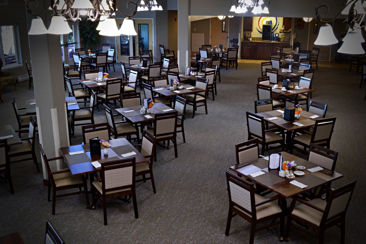 An empty dining room with neatly arranged tables and chairs, illuminated by chandeliers.