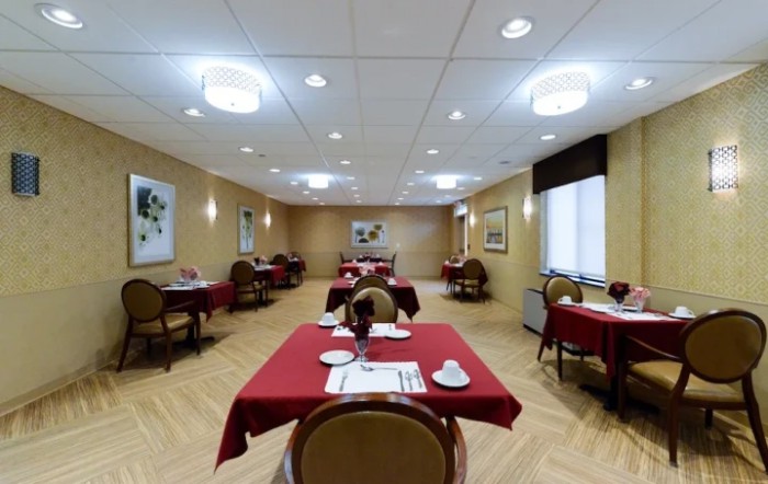 An empty dining room with neatly arranged tables covered in red tablecloths.