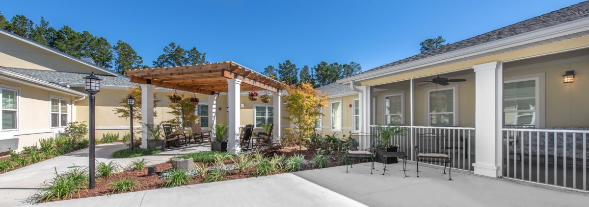 A charming residential patio with a pergola and outdoor seating, surrounded by well-maintained landscaping under a clear blue sky.