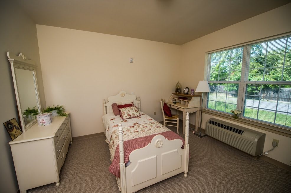 A cozy bedroom featuring a single bed, desk, and dresser with a window view.
