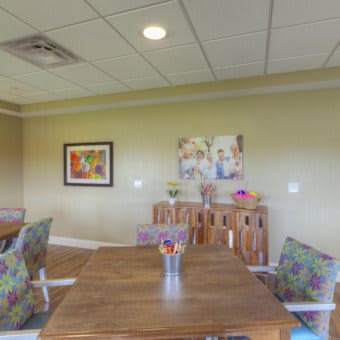 A cozy meeting room with a wooden table, colorful chairs, and decorative artwork on the wall.