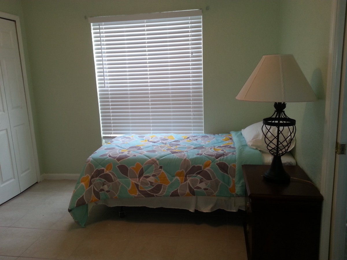 A cozy bedroom with a single bed and a bedside lamp next to a window.
