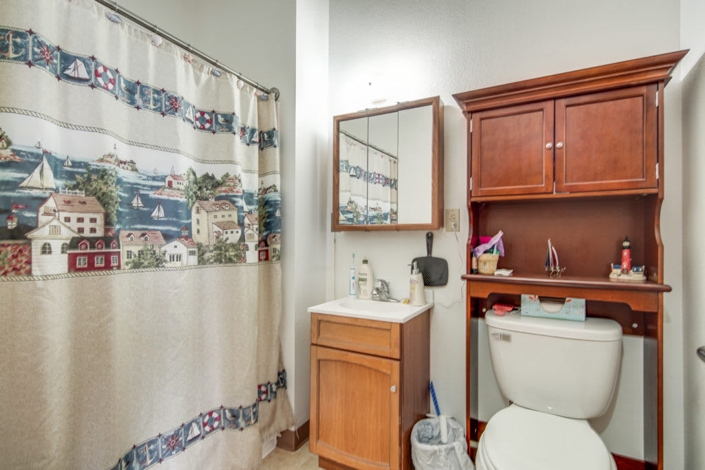 A small bathroom with a shower curtain, sink, mirror, and toilet.