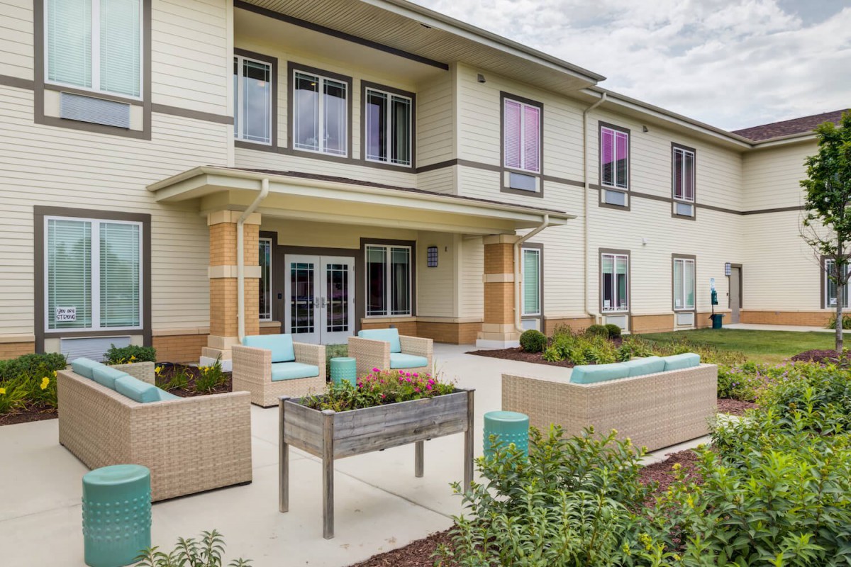 A modern two-story building with a landscaped outdoor seating area and large windows.