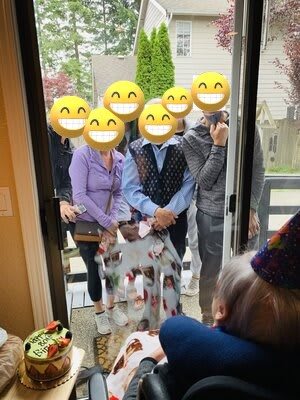 A group of people with emoji-covered faces stand outside a door during a celebration.