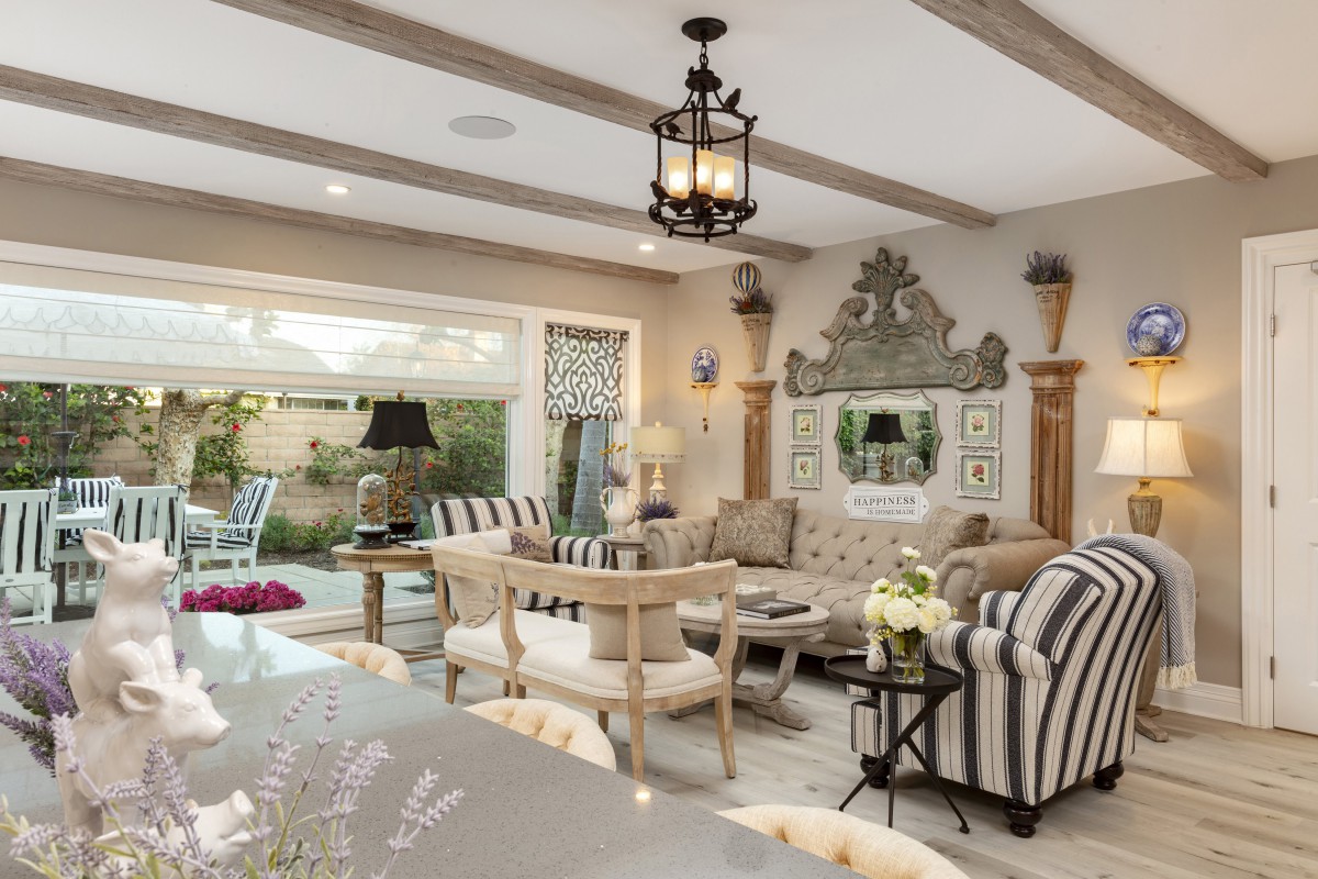 A traditionally styled living room with elegant furniture and decor, featuring a chandelier and large windows opening to an outdoor area.