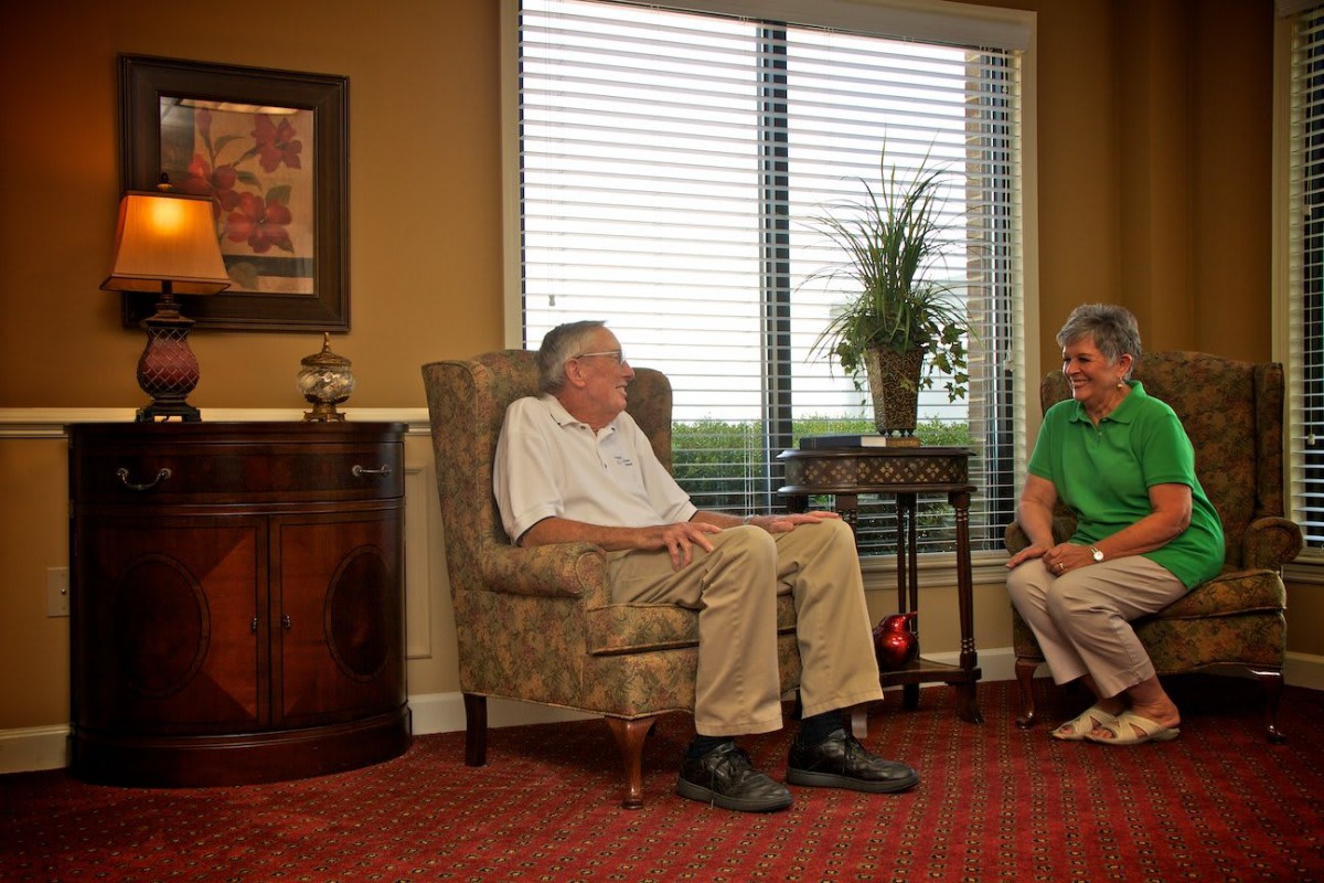 Two seniors are sitting in a cozy living room, engaged in conversation.