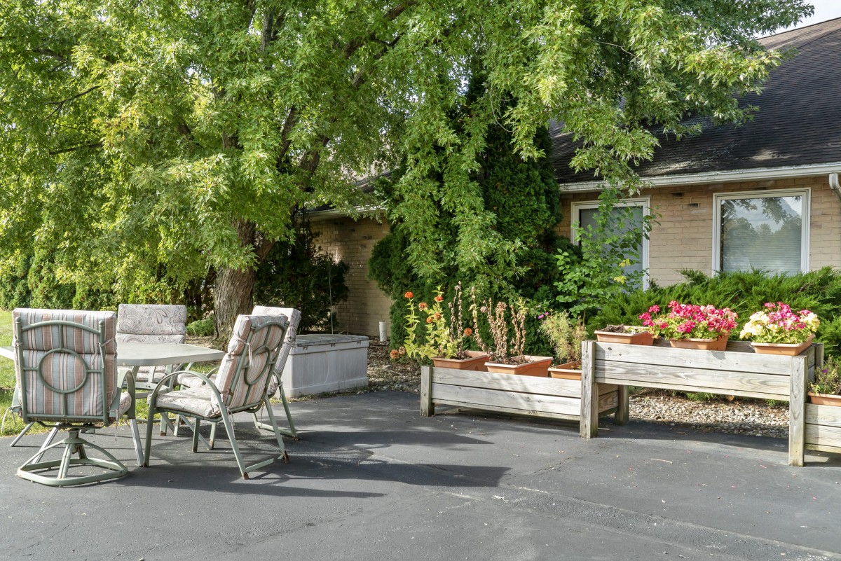 A cozy patio area with outdoor furniture surrounded by lush greenery and flower beds.