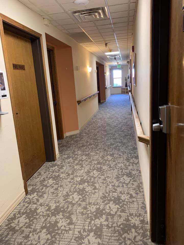 A long, carpeted hallway with multiple doors and overhead lighting.