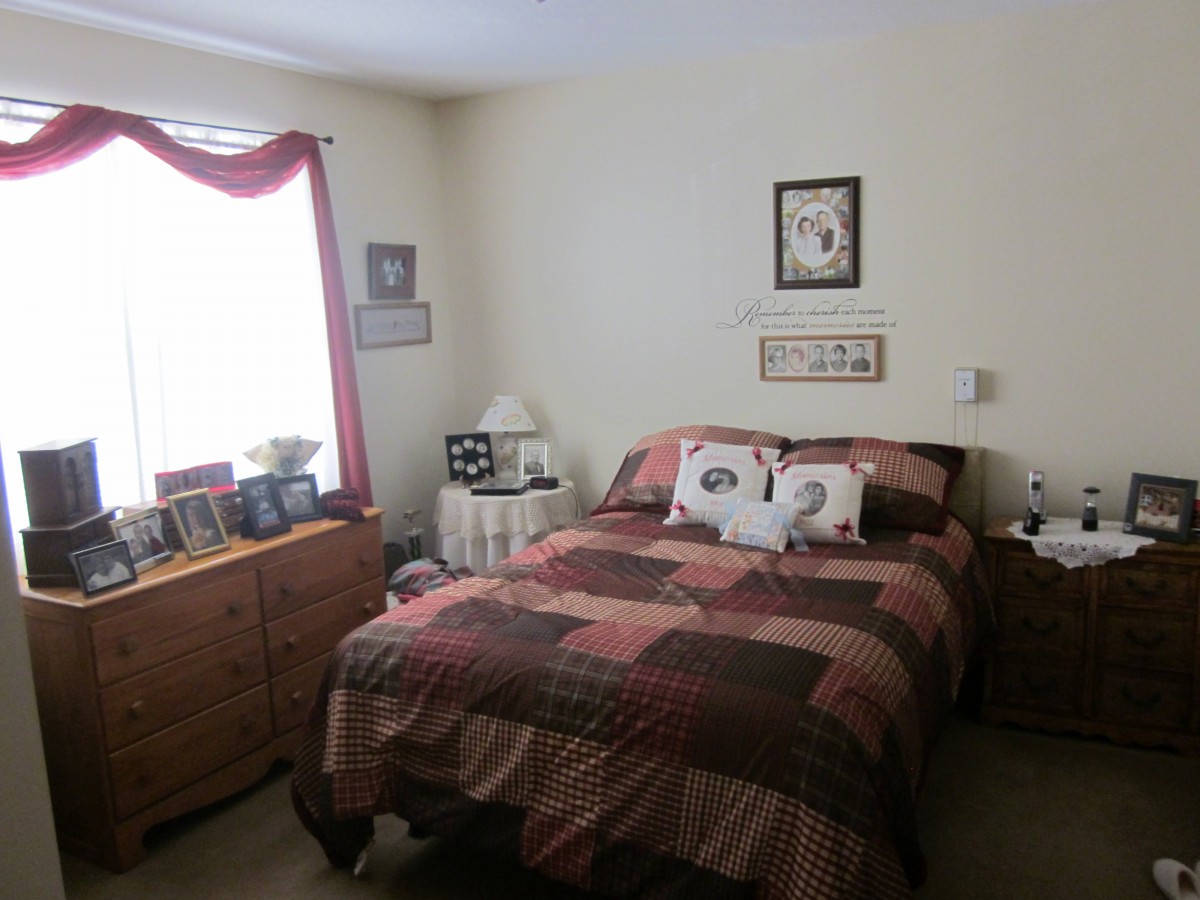 A cozy bedroom with a bed, dresser, and window with red curtains.