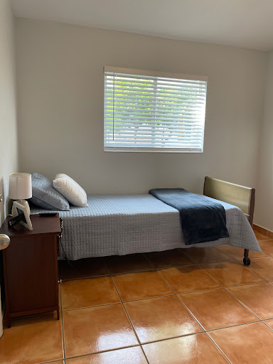 A cozy and minimalist bedroom featuring a single bed, bedside lamp, and a bright window.