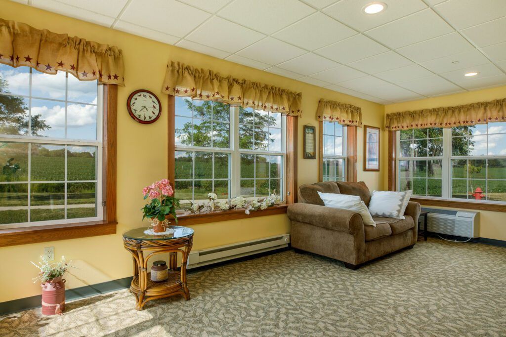 A cozy living room with large windows, a sofa, and decor elements including a clock and plants.