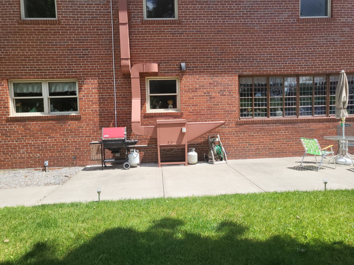A sunny backyard with a brick building, featuring a grill and patio area.