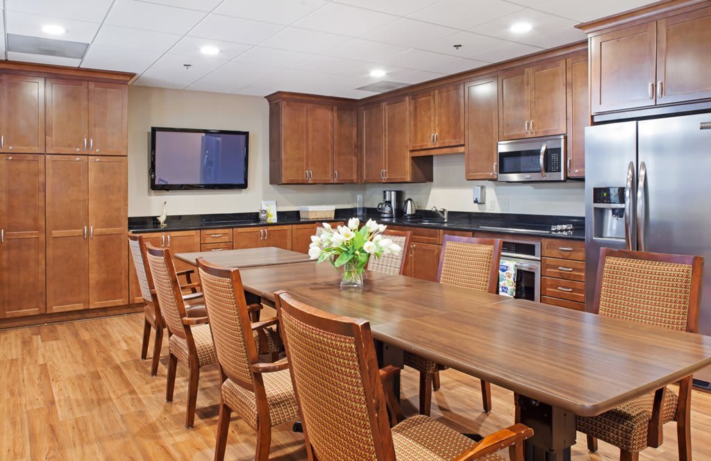 A modern kitchen and dining area featuring wooden cabinets, a large table with chairs, and decorative flowers.