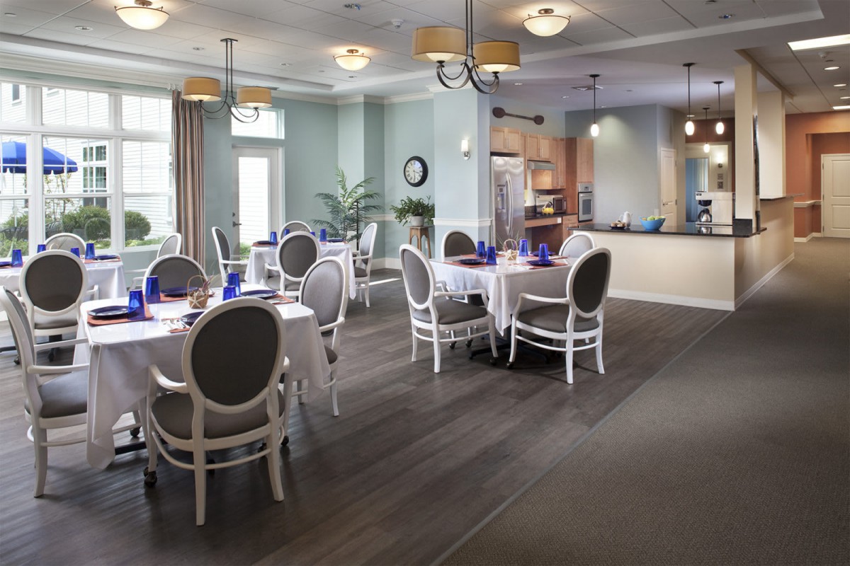 An elegant dining room with neatly arranged tables and chairs, featuring chandeliers and a wooden floor.