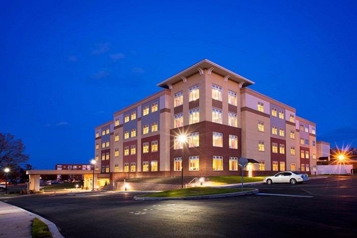 A well-lit building at night with a clear sky and a parking area in the foreground.