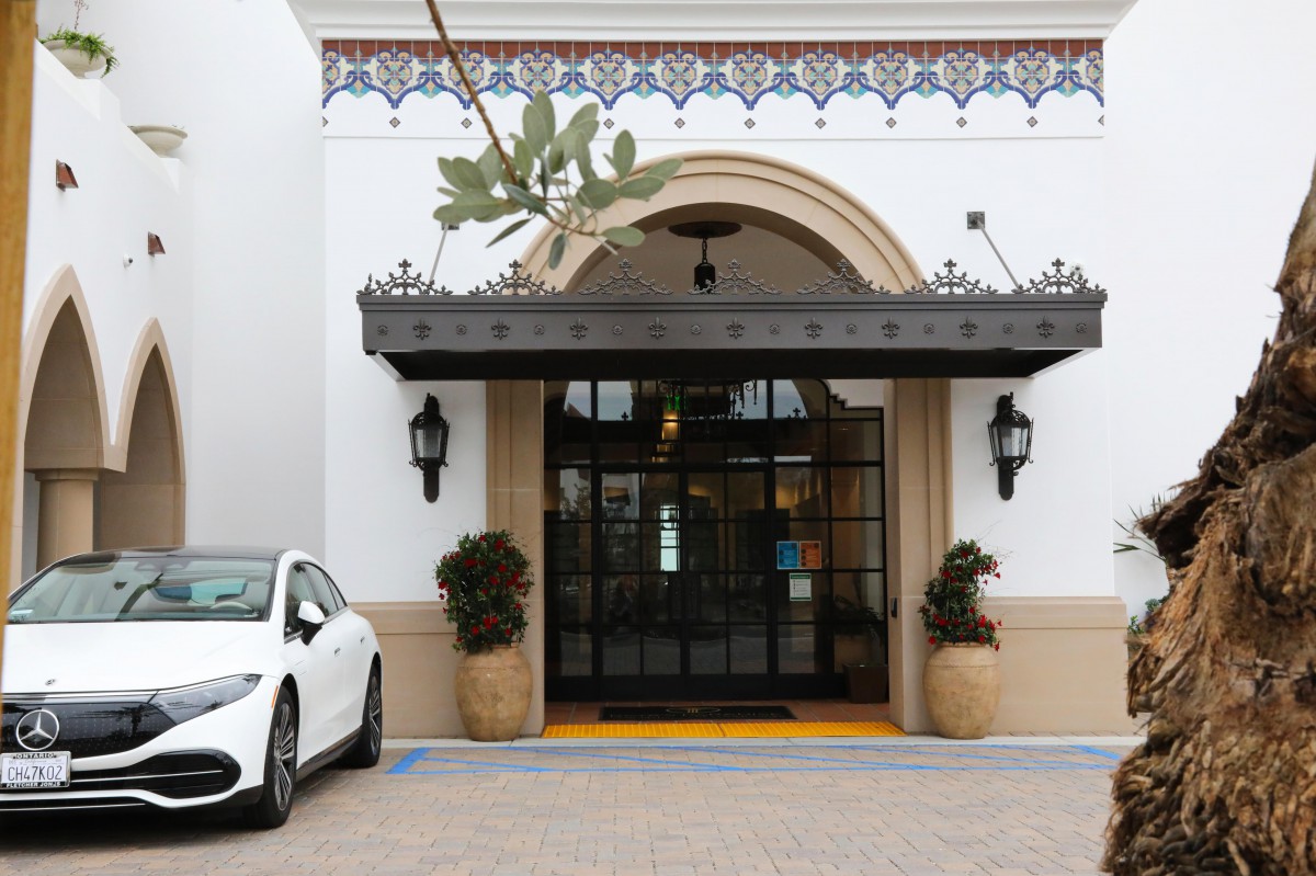 A Mediterranean-style building entrance with a car parked nearby and potted plants on either side of the doorway.