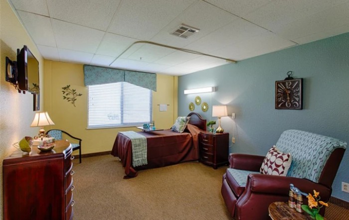 A cozy bedroom with a single bed, armchair, and nightstand.