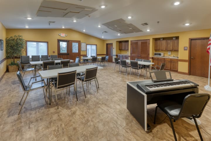 A spacious community center meeting room with tables, chairs, and a kitchen area.