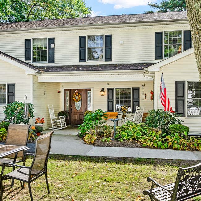 A charming two-story house with a manicured garden and patio furniture in the front yard.