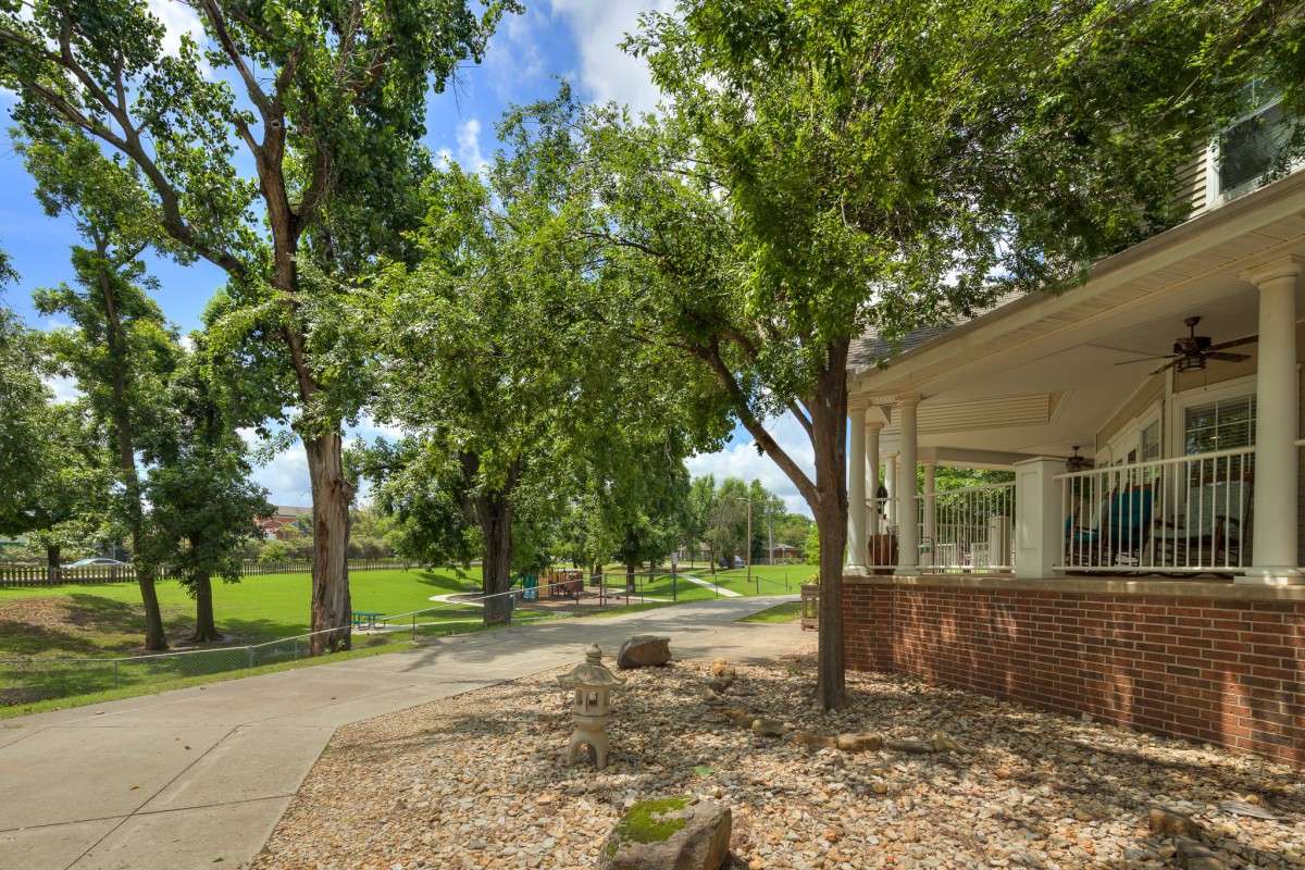 A tranquil park scene with a pathway bordered by lush green trees and a building on the right.