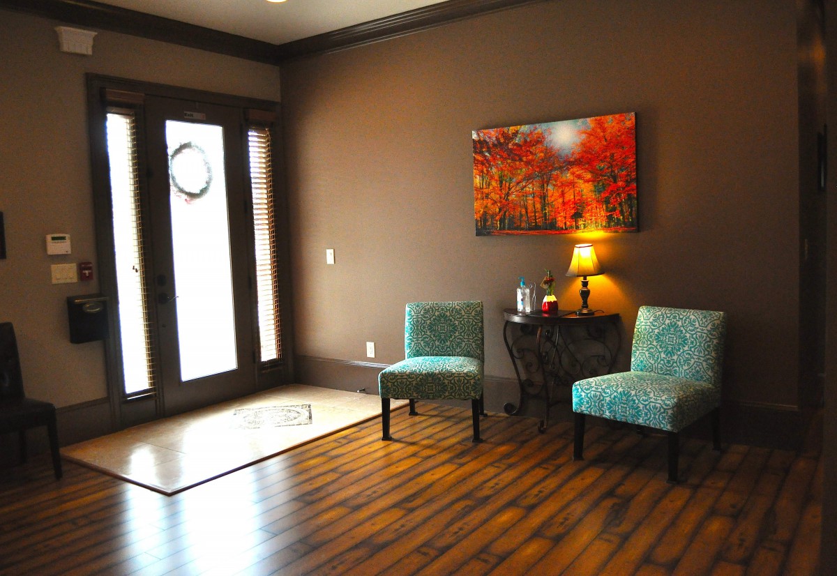 A cozy waiting room with teal chairs, a small table with a lamp, and colorful artwork on the wall.