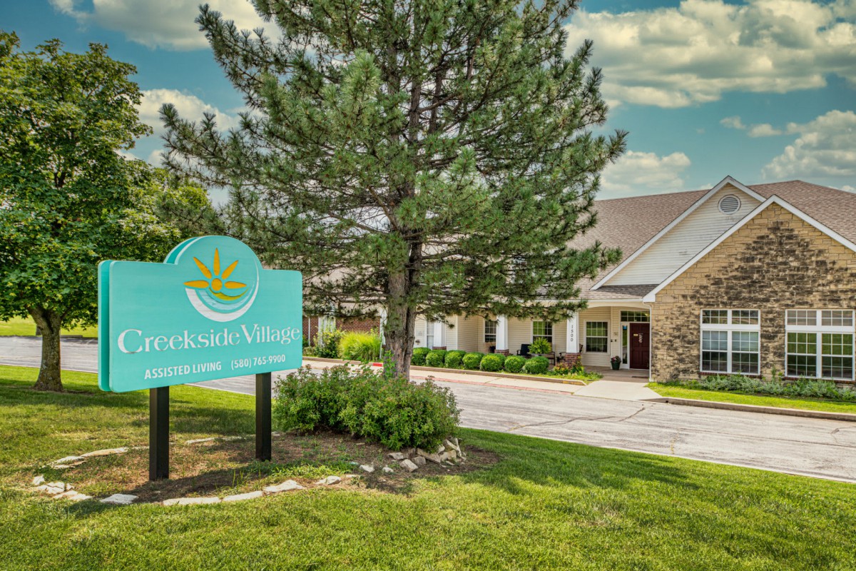 A serene building exterior with a sign and lush greenery under a partly cloudy sky.