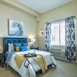 A modern bedroom with a blue and white color scheme, featuring a comfortable bed, stylish artwork, and patterned curtains.