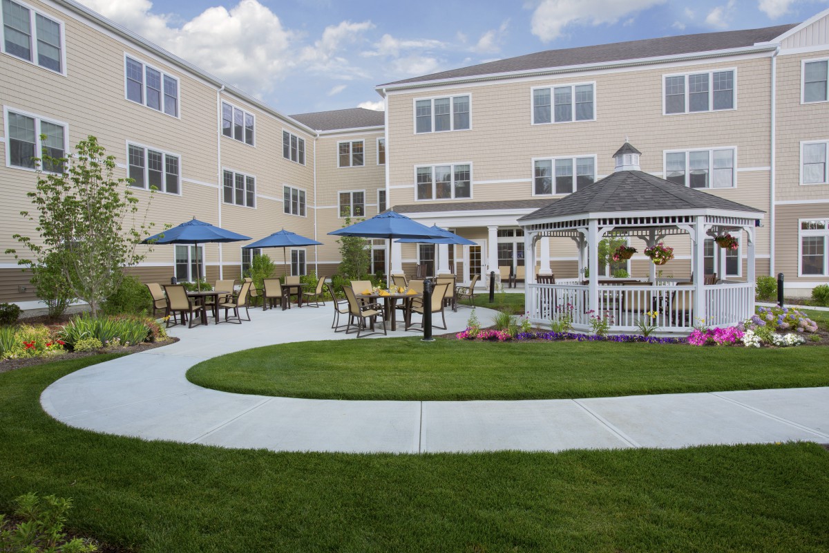 A well-maintained courtyard with outdoor seating, umbrellas, and a gazebo in front of a multi-story building.