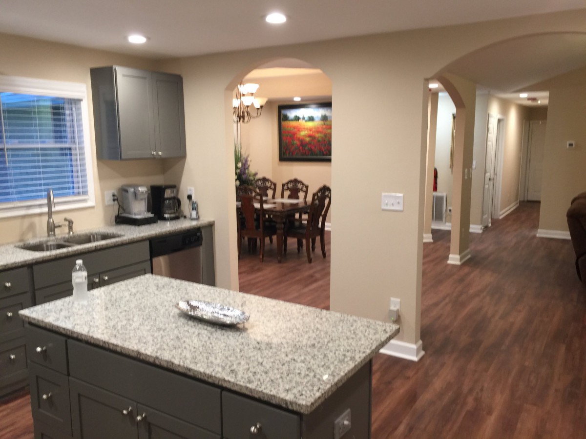 A modern kitchen with an island and adjacent dining area, featuring open space and wood flooring.