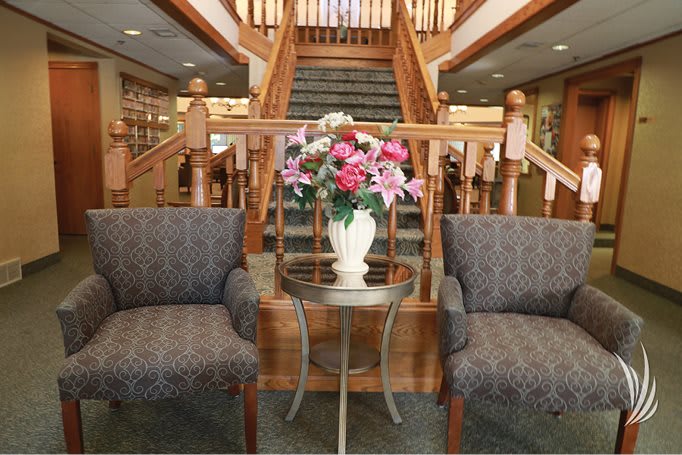 A lobby area with two chairs and a table with a flower vase, set in front of a wooden staircase.