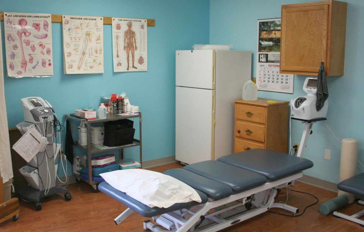 A medical examination room with a treatment table, anatomical charts, and various medical supplies.