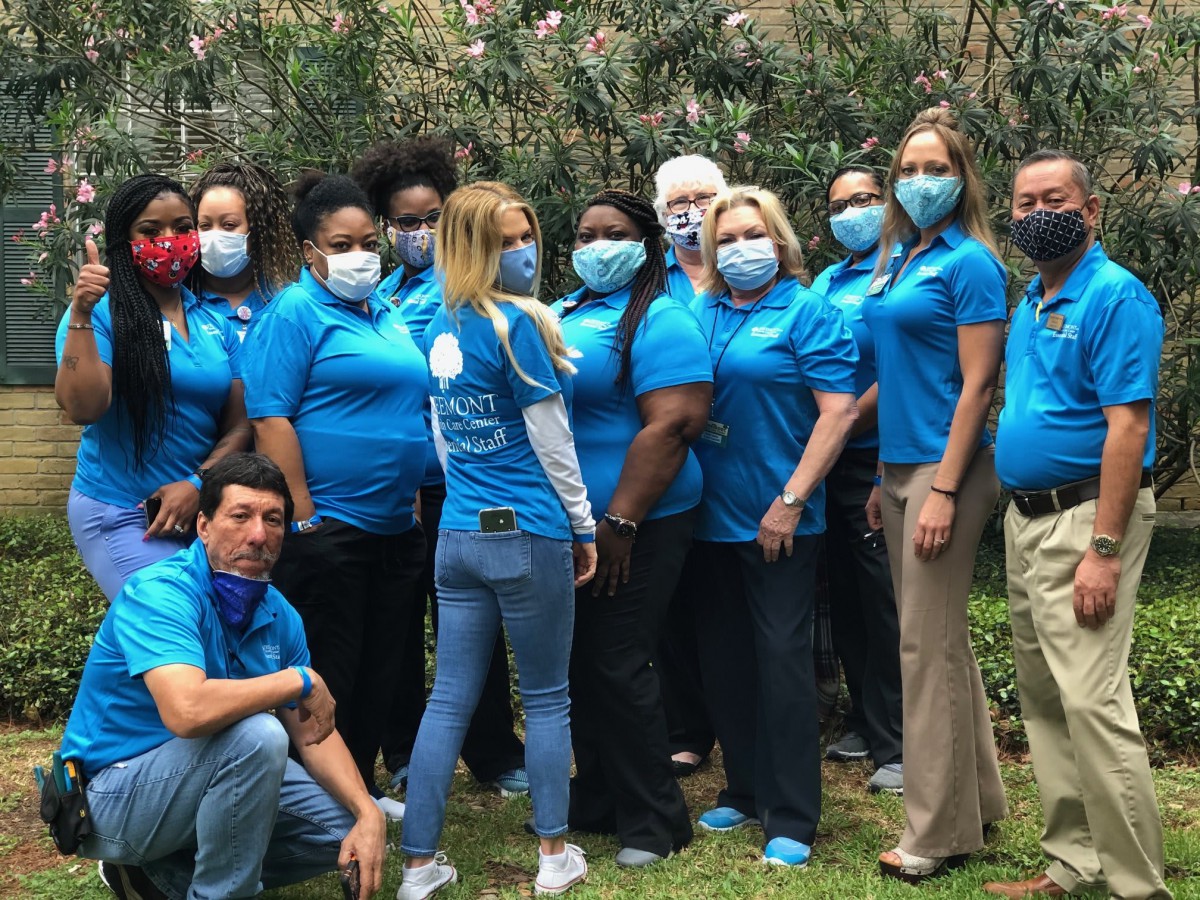 A group of people wearing matching blue shirts and masks, posing outdoors.