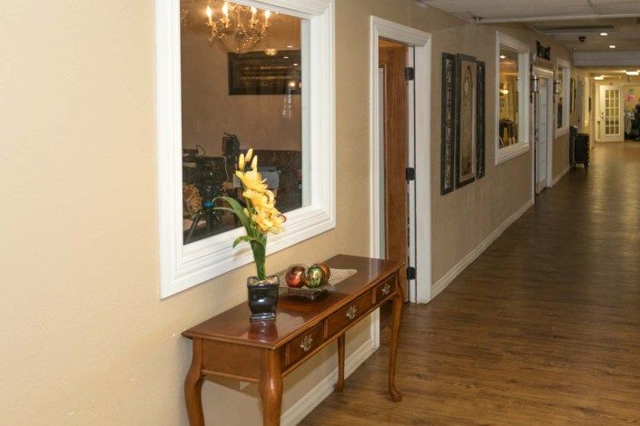 A hallway with a wooden table, decorative flowers, and mirrors on the wall.