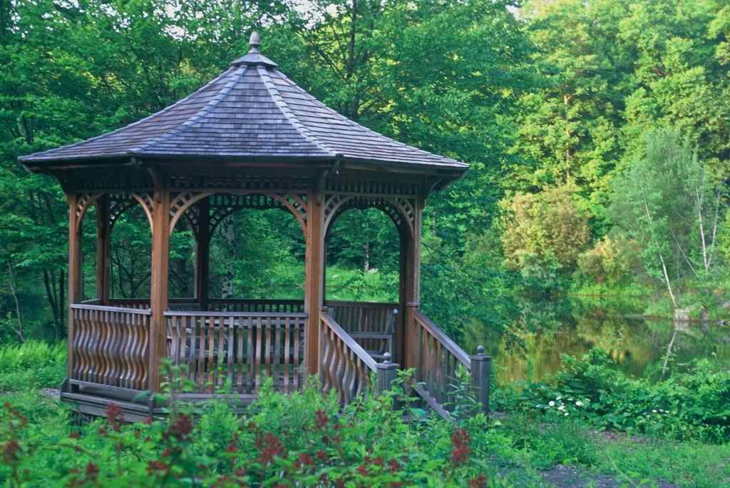 A wooden gazebo surrounded by lush greenery in a garden setting.