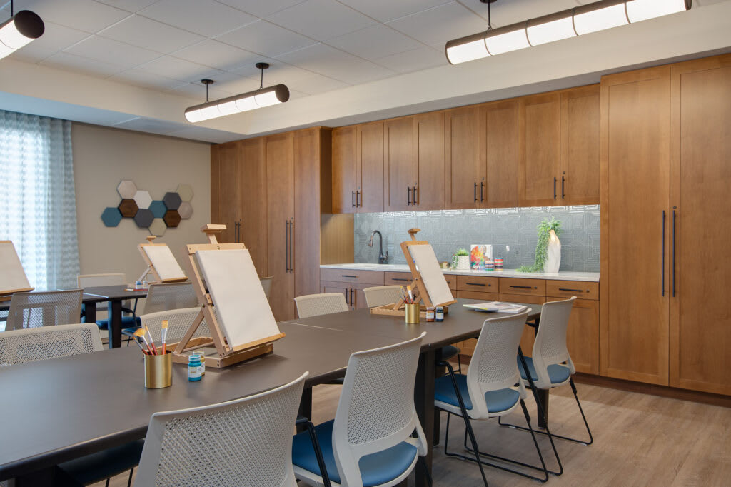 A modern art studio with easels set up on tables, surrounded by chairs and wood cabinetry.