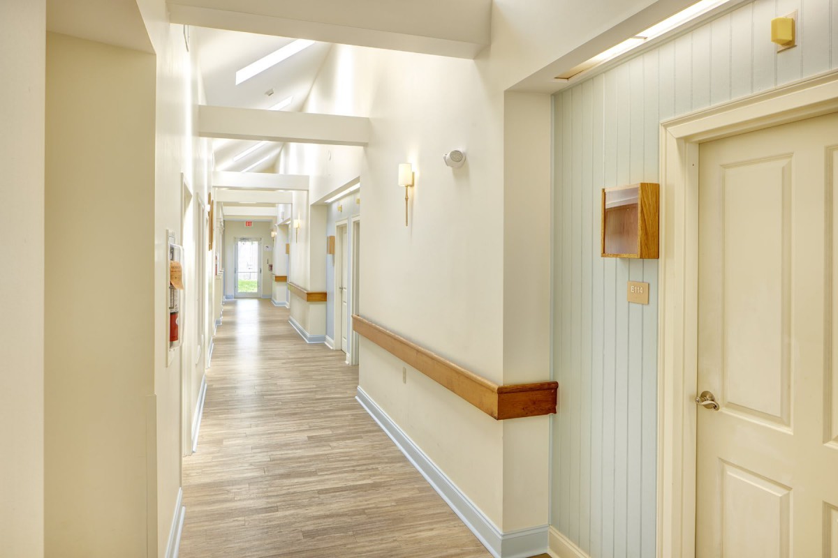 A well-lit hallway with wooden flooring and cream-colored walls, featuring doors and wall-mounted lights.