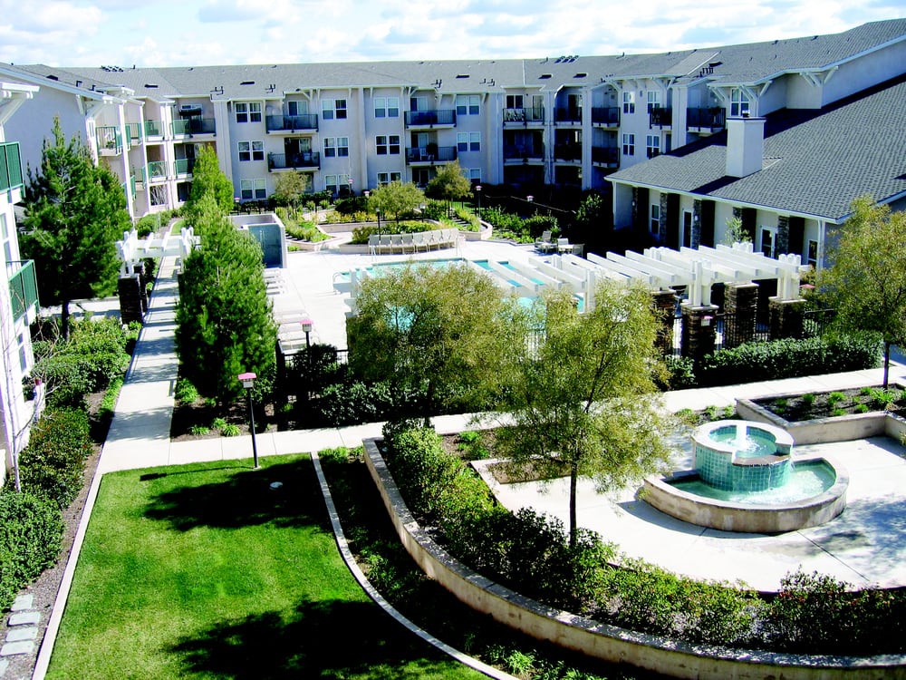 A modern apartment complex featuring a courtyard with a pool and fountain surrounded by lush landscaping.