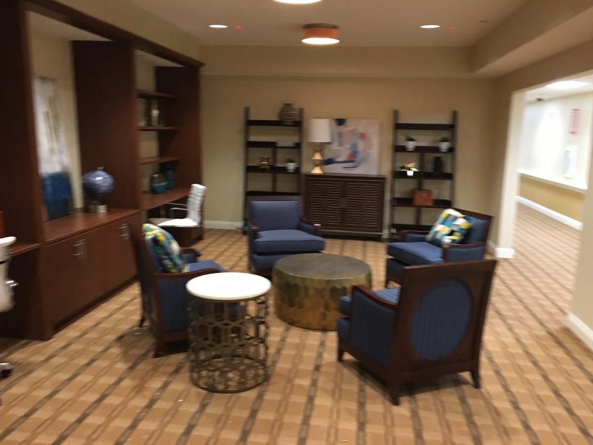 A cozy lounge area with blue chairs and round tables, surrounded by bookshelves and a carpeted floor.