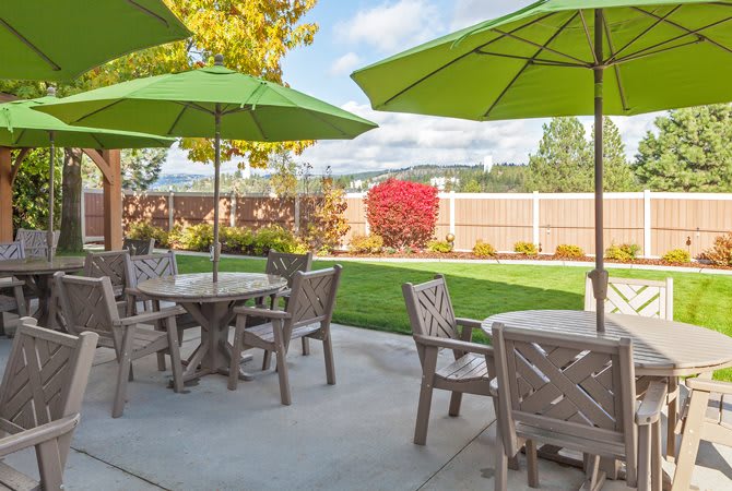 A sunny backyard patio with tables and chairs under green umbrellas.