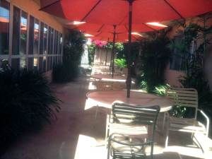 A sunny outdoor patio with red umbrellas, chairs, and tables.