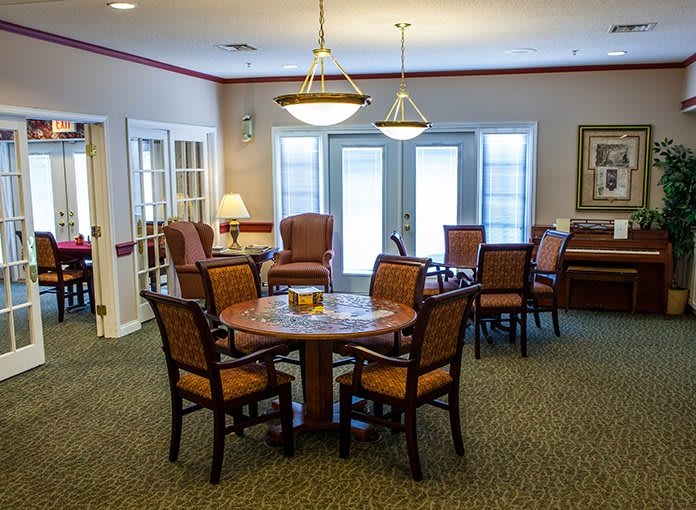 A cozy dining area with a round table surrounded by chairs, featuring warm lighting and natural light from nearby windows.